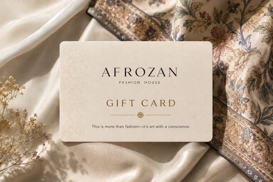 An Afrozan fashion house gift card with elegant black and gold lettering, styled on a draped cream silk fabric with a floral scarf in the background.
