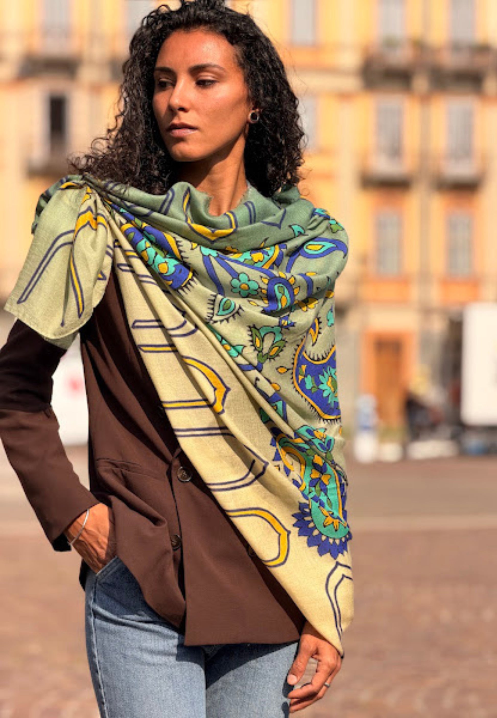 Woman wearing a large patterned scarf outdoors with blurred buildings in the background
