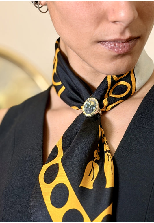 A close-up of a model wearing a black silk scarf with a pari-dar pattern and silver ring with the same pattern
